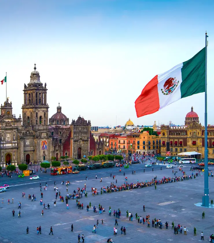 Plaza central con catedral, bandera de M&eacute;xico ondeando y grupos de personas alrededor.