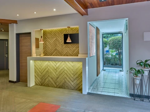 Recepci&oacute;n moderna con paredes de madera, luces colgantes y pasillo hacia un jard&iacute;n exterior.