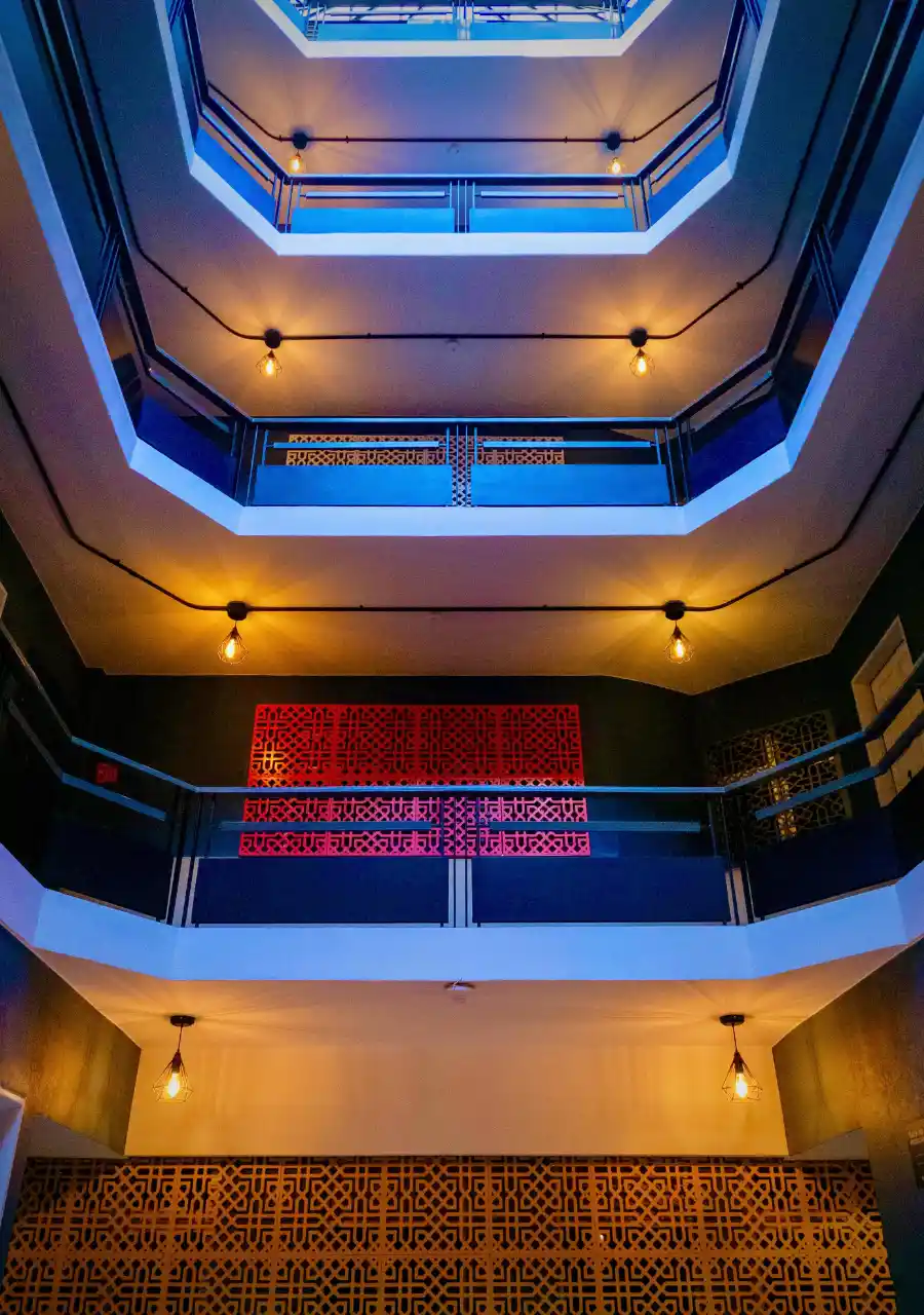 Interior de edificio con balcones y luces &aacute;mbar, decorado con paneles geom&eacute;tricos en azul y rojo.