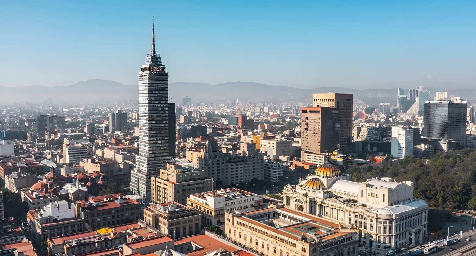 Panor&aacute;mica de ciudad con rascacielos; destaca edificio con c&uacute;pula dorada y monta&ntilde;as al fondo.