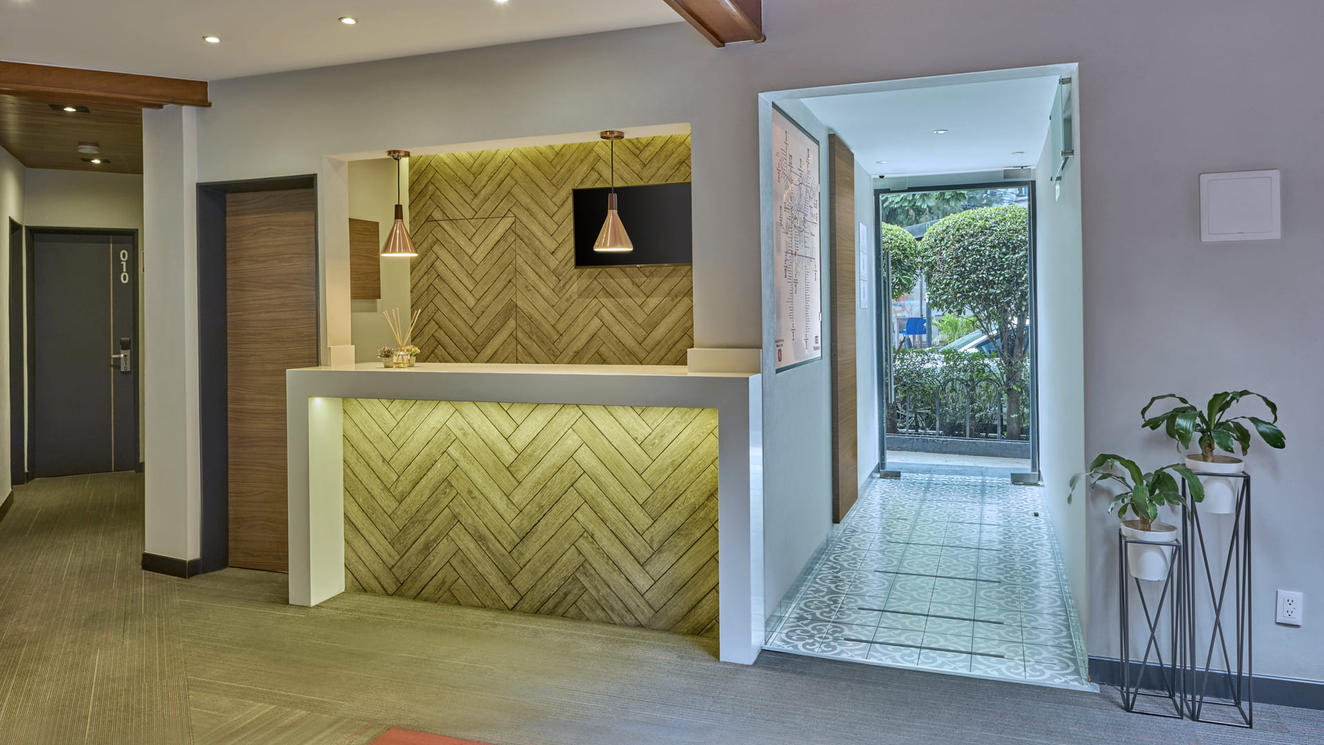 Recepci&oacute;n moderna con pared de madera, l&aacute;mpara colgante y plantas decorando la entrada iluminada.