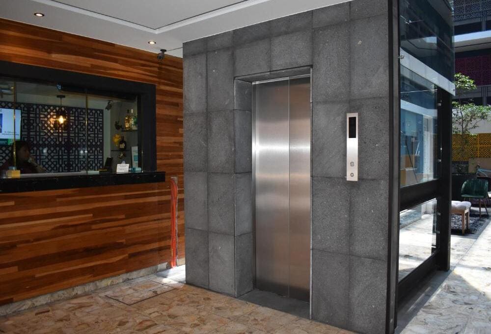 Ascensor de paredes grises junto a recepci&oacute;n con dise&ntilde;o de madera en un entorno moderno y luminoso.