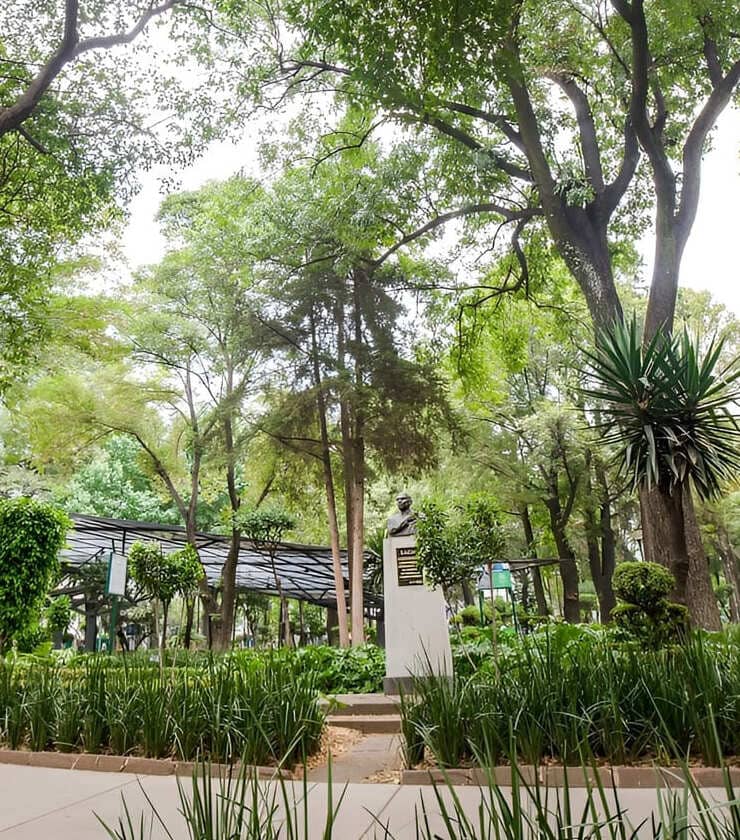 Parque con busto en pedestal rodeado de &aacute;rboles y plantas.