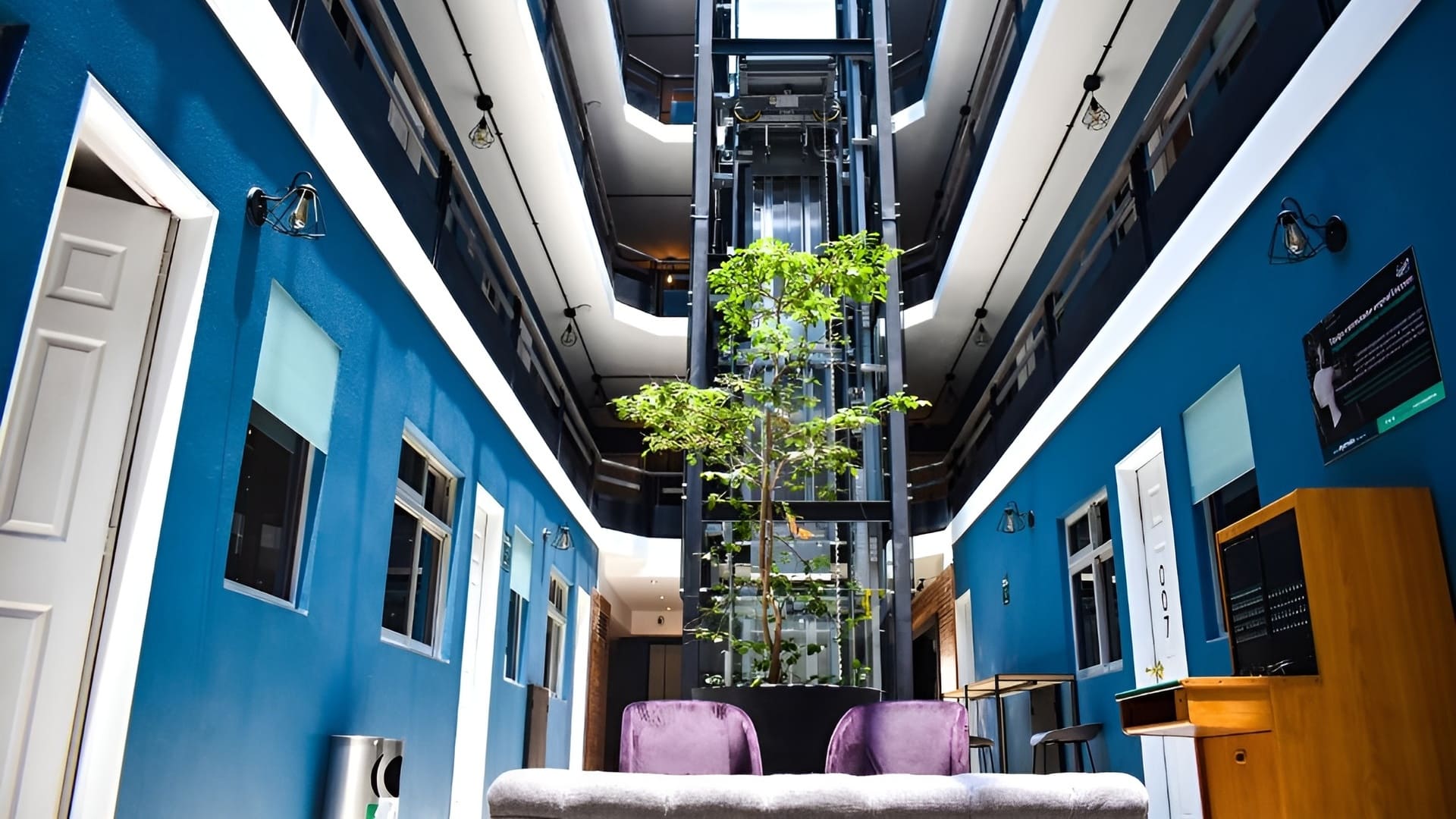 Interior moderno con paredes azules, plantas y un ascensor visible al fondo.