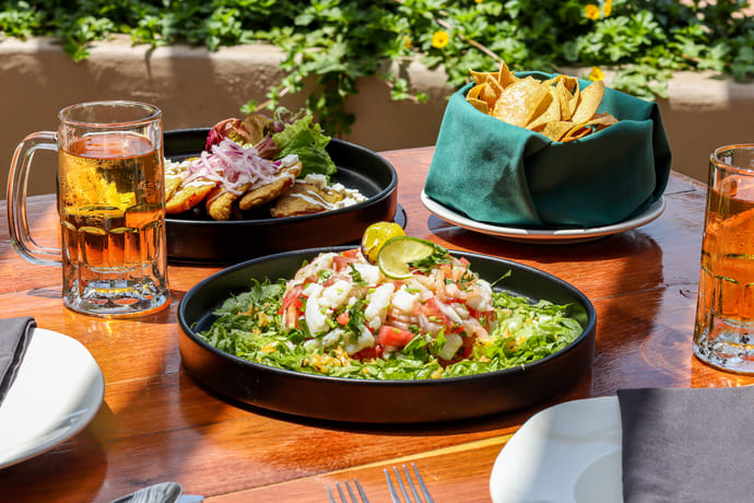 Platos de comida mexicana con ceviche, totopos y cervezas sobre una mesa de madera al aire libre.