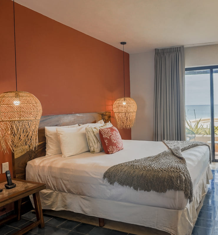 Habitación moderna con cama grande, lámparas colgantes de mimbre, y ventanal con vista al mar.