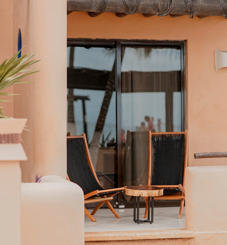 Dos sillas de madera y una mesa pequeña en una terraza junto a una puerta corrediza de vidrio.