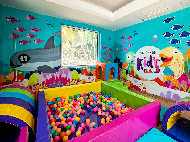 Sala de juegos infantil con piscina de pelotas y paredes decoradas con dibujos de peces y océano.