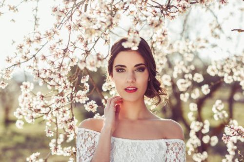 Mujer con vestido blanco de encaje entre flores de cerezo, al aire libre, con expresión serena.