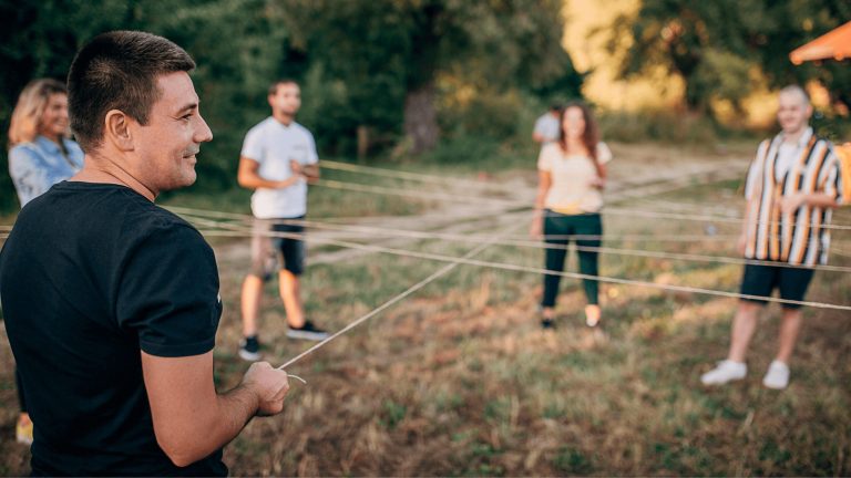 Personas participan en una actividad al aire libre, sosteniendo cuerdas en círculo sobre césped verde.