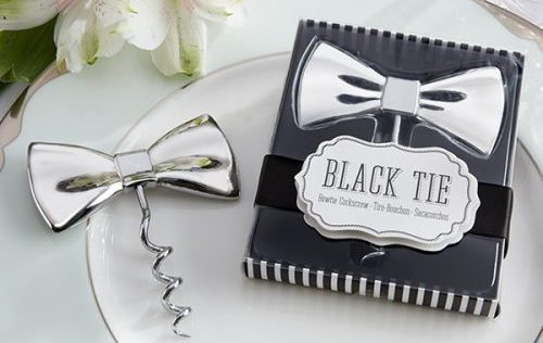 Sacacorchos con forma de corbata de lazo plateada junto a una caja de regalo "Black Tie" en una mesa elegante.