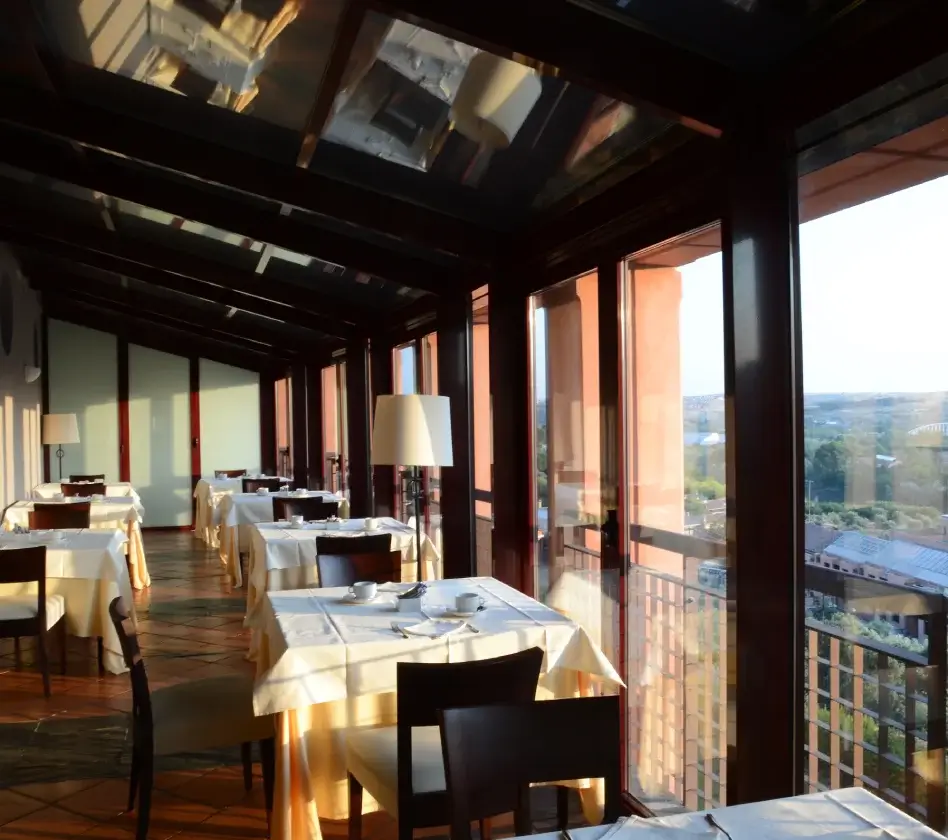 Comedor elegante con mesas cubiertas de manteles blancos y grandes ventanas que dejan entrar luz natural.