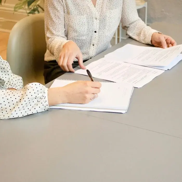 Personas revisando papeles y tomando notas en una reunión sobre una mesa gris.