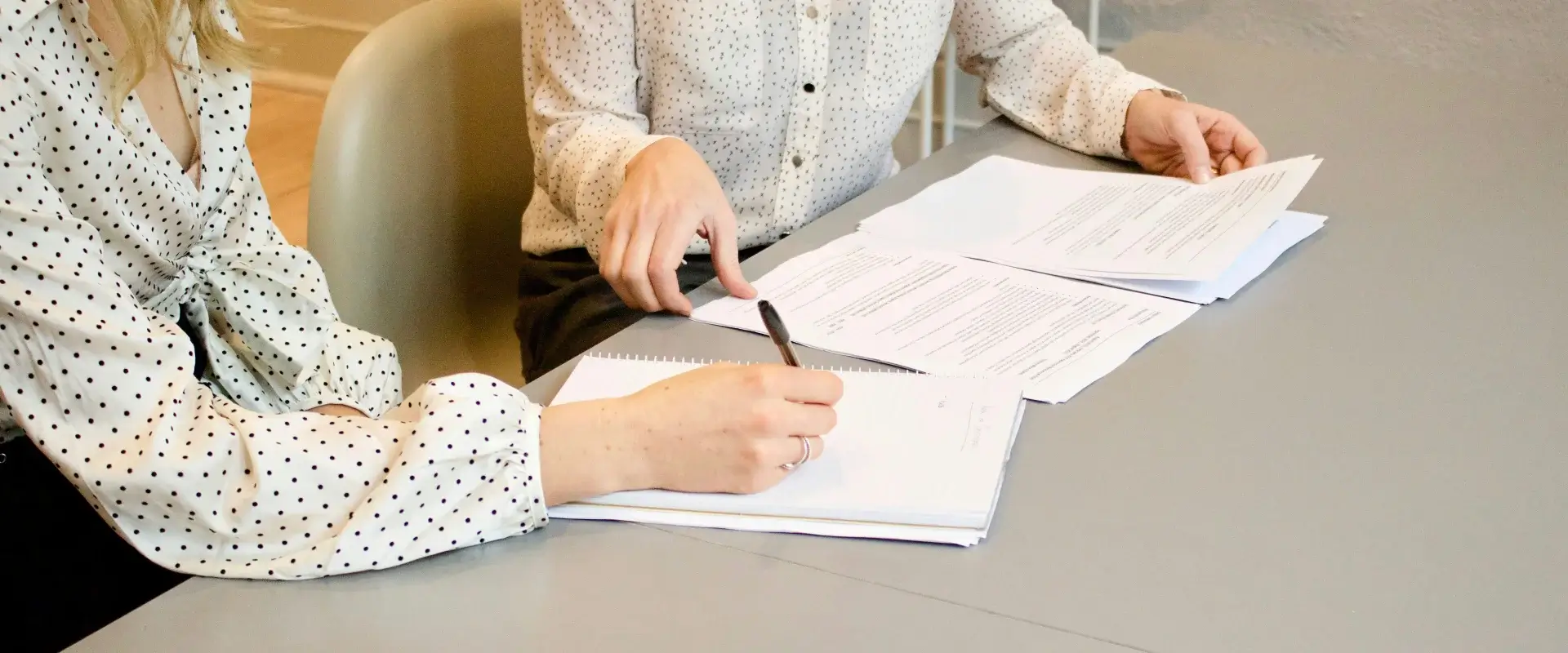 Dos personas revisan documentos en una mesa, ambas visten camisas de lunares.