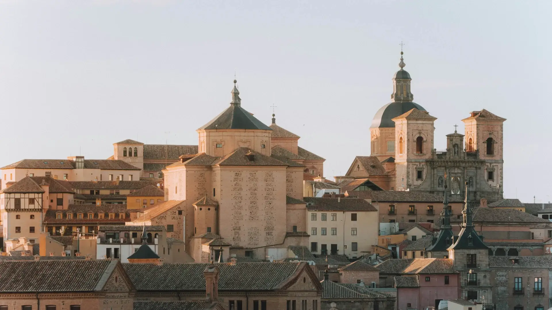 Vista de una ciudad antigua con edificios de estilo clásico y cúpulas, bajo un cielo despejado al atardecer.