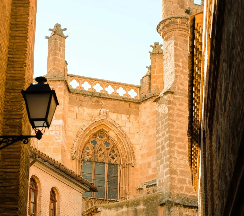 Antigua iglesia de piedra con arco gótico, torreones y ventana ornamentada vista desde una calle estrecha.