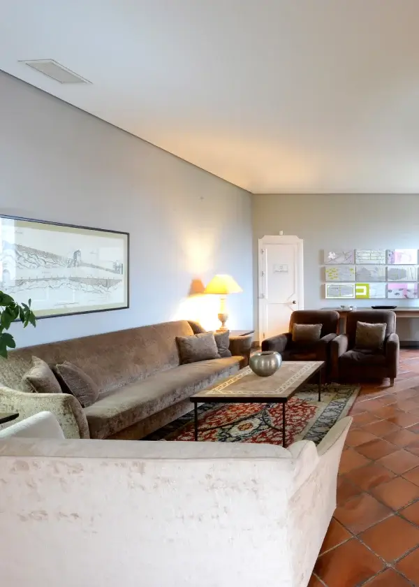 Sala de estar con sofá, sillones, lámpara encendida, mesa decorativa y cuadros en el muro, con luz natural entrando.