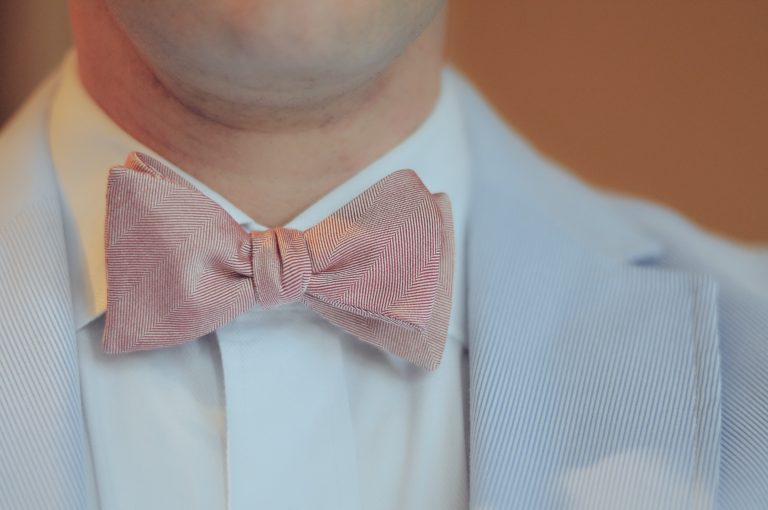 Hombre con traje azul claro, camisa blanca y moño rosa con patrón de espiga.