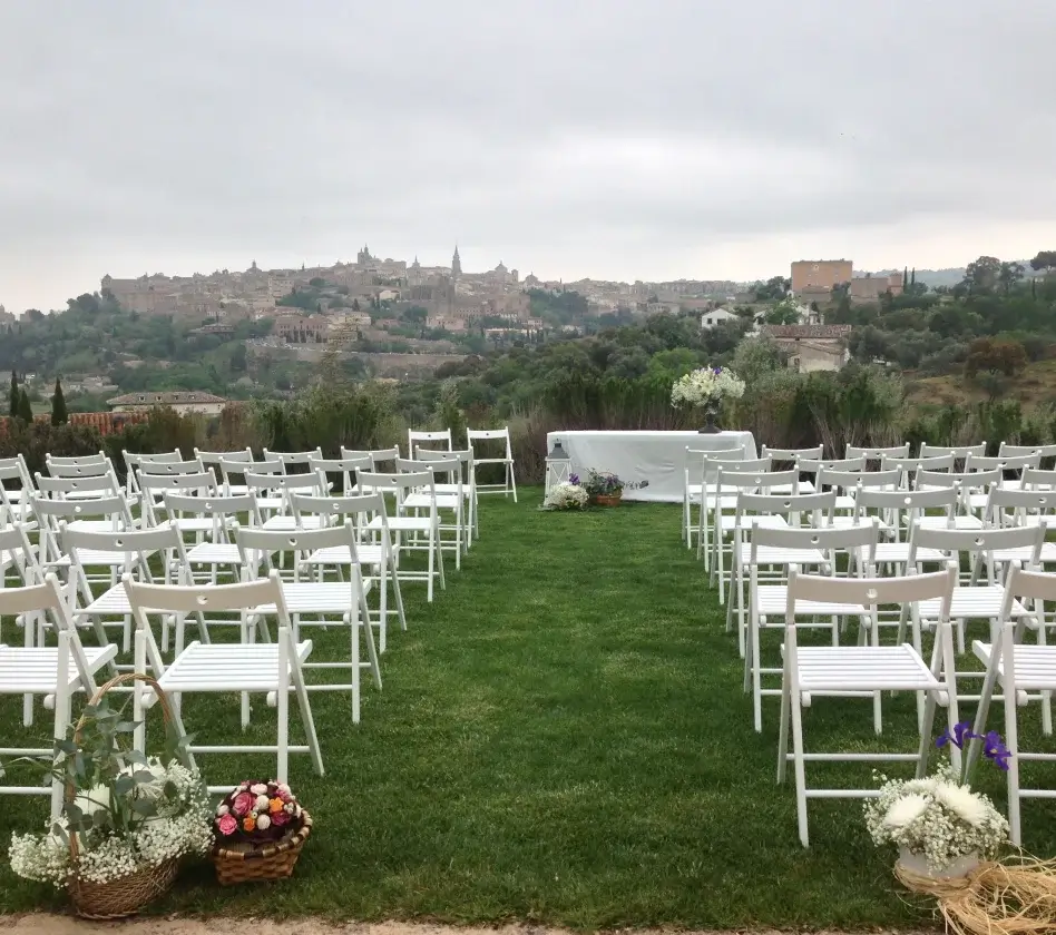 Ceremonia al aire libre con sillas blancas, decoración floral y una vista panorámica de una ciudad al fondo.