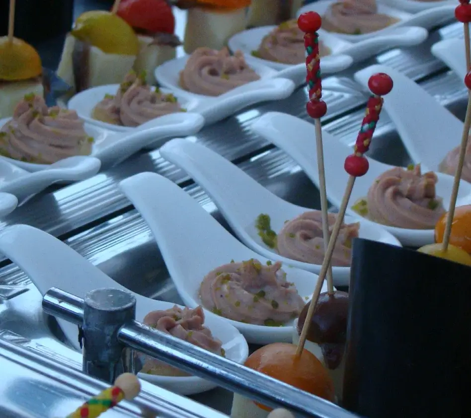 Bandeja de bocadillos gourmet, con crema rosa en cucharas blancas y brochetas decorativas.