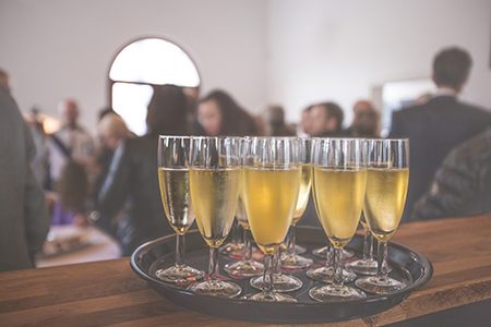Vasos de champán en una bandeja sobre una mesa de madera, con personas borrosas en el fondo en un evento.