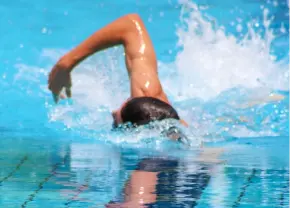 Persona nadando estilo libre en una piscina, con el brazo levantado y salpicaduras de agua alrededor.