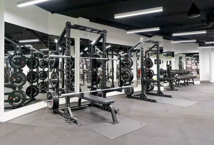 Gimnasio moderno con máquinas de pesas, incluyendo bancos y discos. Ambiente limpio y bien iluminado.