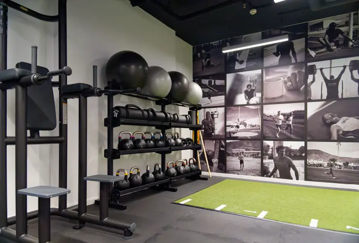 Gimnasio con kettlebells, pelotas de ejercicio y un mural de fotos deportivas; área con césped artificial.