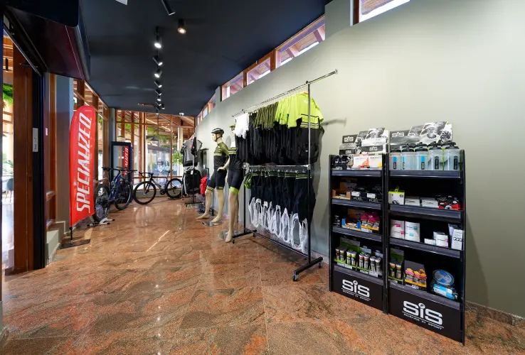 Tienda de ciclismo con maniquíes, ropa deportiva, suplementos y bicicletas en exhibición sobre un piso de mármol.