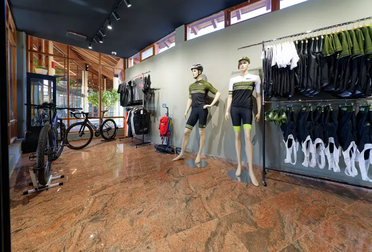 Tienda de ciclismo con maniquíes, bicicletas, ropa y accesorios en exhibición en un piso de mármol brillante.