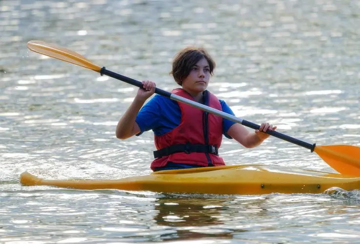 Persona en kayak amarillo con chaleco salvavidas rojo, remando en el agua.