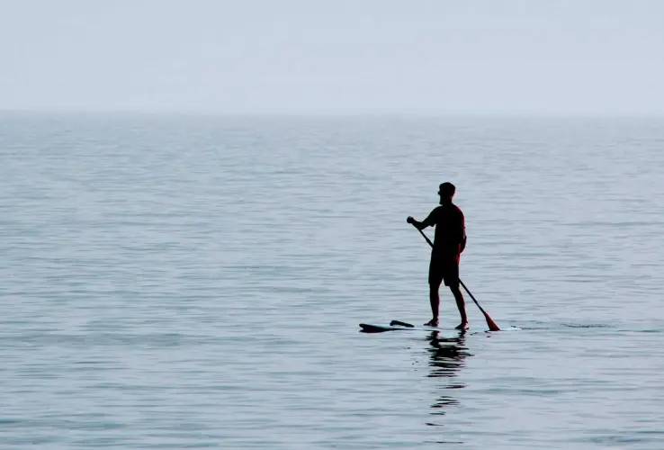 Persona practicando paddleboarding en un lago tranquilo bajo un cielo despejado.