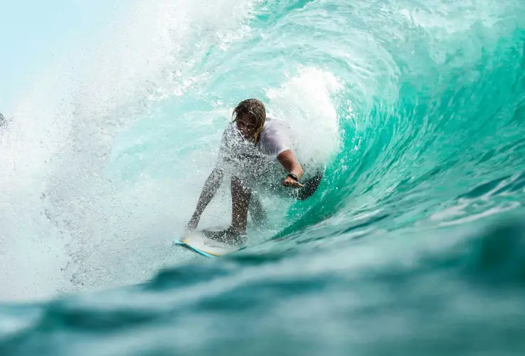 Surfero dentro de un tubo de agua turquesa, surfeando con destreza en una gran ola.