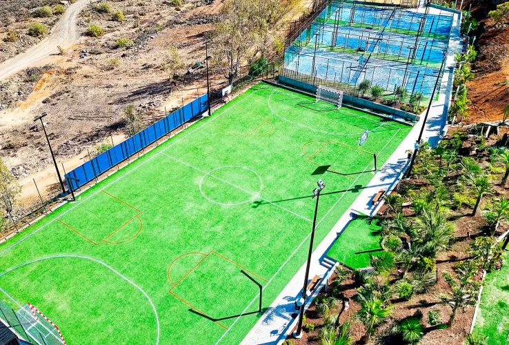 Campo de fútbol y canchas de pádel al aire libre, rodeados de vegetación y caminos, vistos desde arriba.