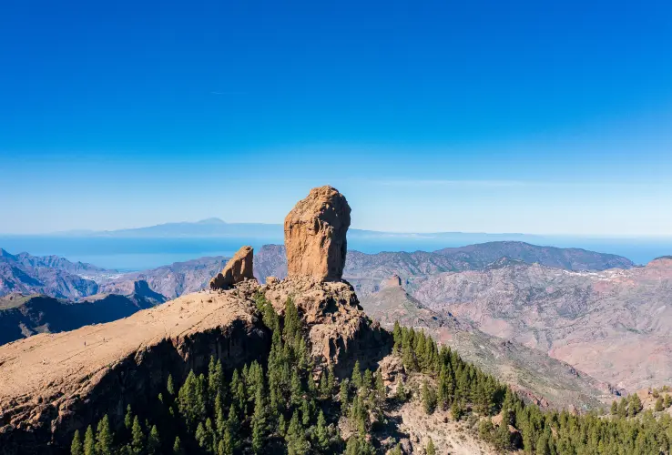 Formación rocosa en un paisaje montañoso con cielo azul y vegetación en primer plano.