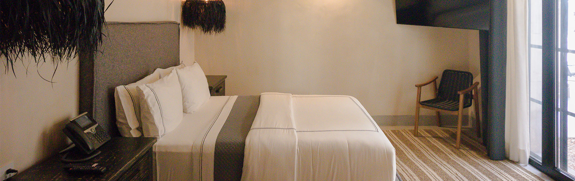Habitación moderna con cama grande, lámparas negras colgantes y una silla junto a una ventana grande con cortinas.