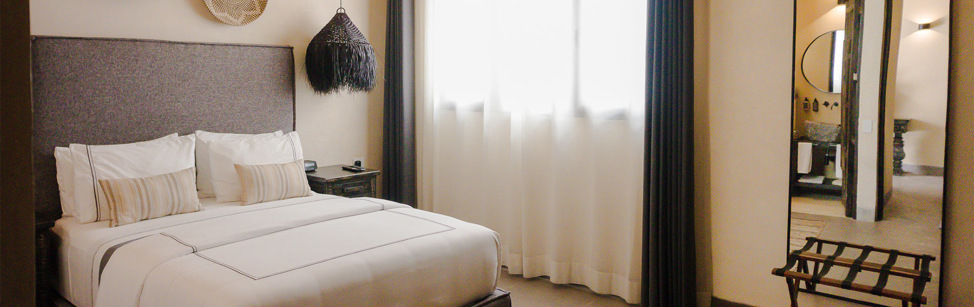 Habitación de hotel elegante con cama doble, lámparas de diseño y un gran espejo junto a la ventana con cortinas claras.
