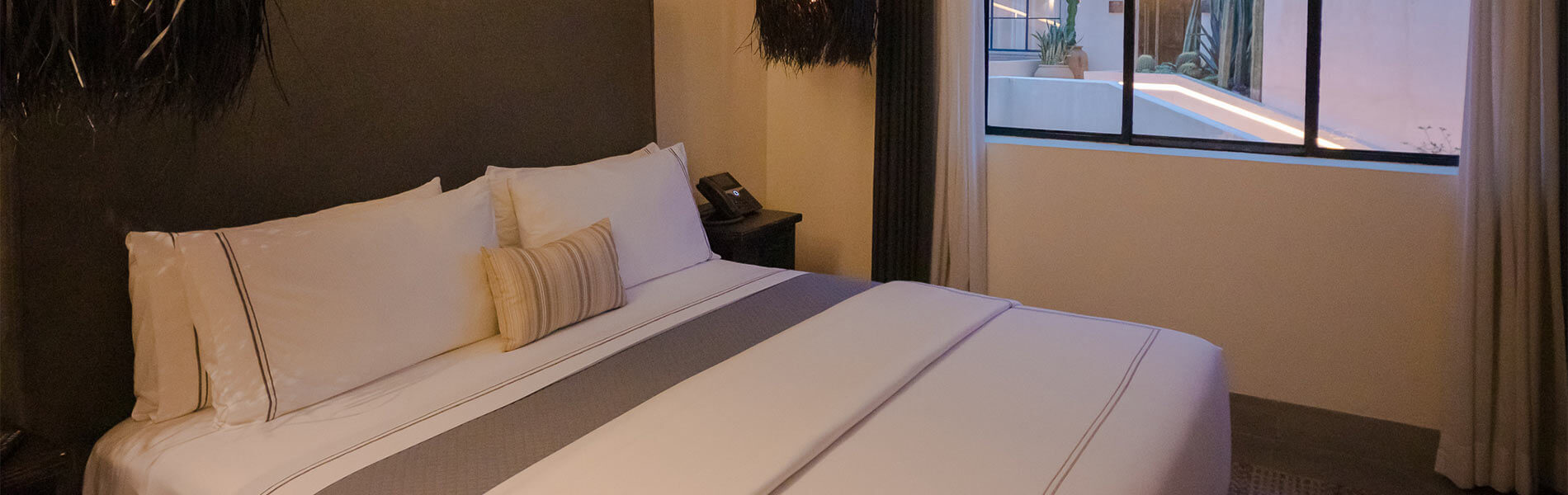 Cama grande en habitación acogedora con ventana, luz tenue y decoración sencilla.