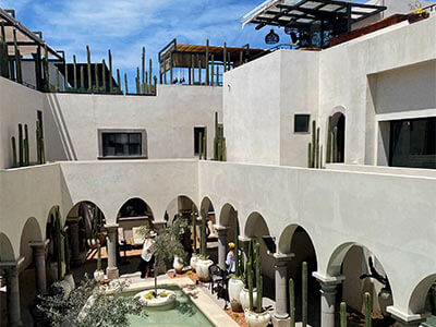 Patio interior con arcos, fuente central y cactus en la terraza. Cielo azul claro arriba.