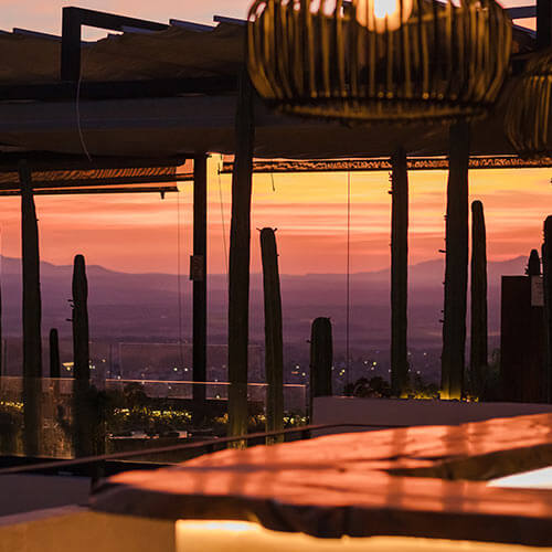 Terraza al atardecer con iluminación cálida y cactos en el horizonte. Vista de un paisaje montañoso.