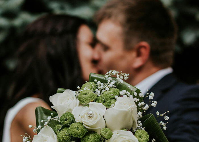 Pareja besándose, con enfoque en un ramo de flores blancas y verdes en primer plano.