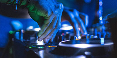 Manos mezclando música en una consola de DJ con luces azules y verdes.