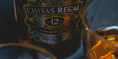 Botella de whisky Chivas Regal de 12 años junto a un vaso con whisky.