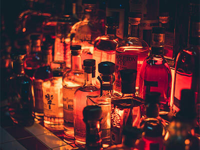 Botellas de licor iluminadas en tonos cálidos, dispuestas en varias filas sobre una superficie.