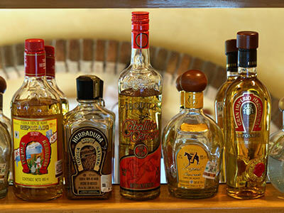 Botellas de tequila de diferentes marcas alineadas sobre un estante de madera.