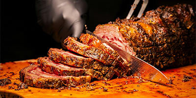 Carne asada siendo rebanada sobre una tabla de cortar, mostrando jugosidad y especias en la superficie.
