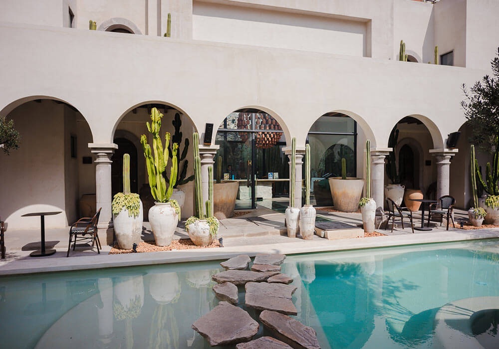 Patio con arcos, plantas en macetas grandes y piscina con piedras, estilo mediterráneo.