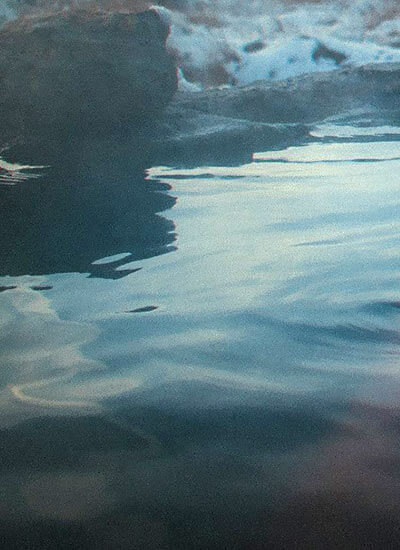 Agua tranquila con reflejos de luz y una roca oscura en el fondo.