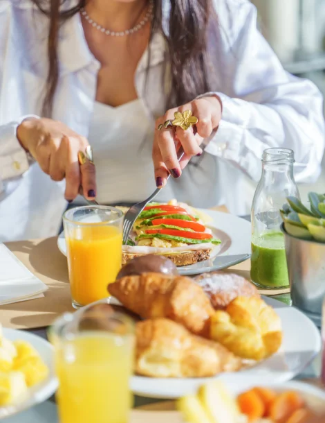 Persona disfrutando un desayuno con jugo, tostada y croissants.