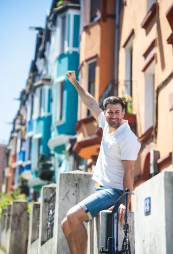 Hombre sonriente con puño levantado, sentado frente a casas coloridas.